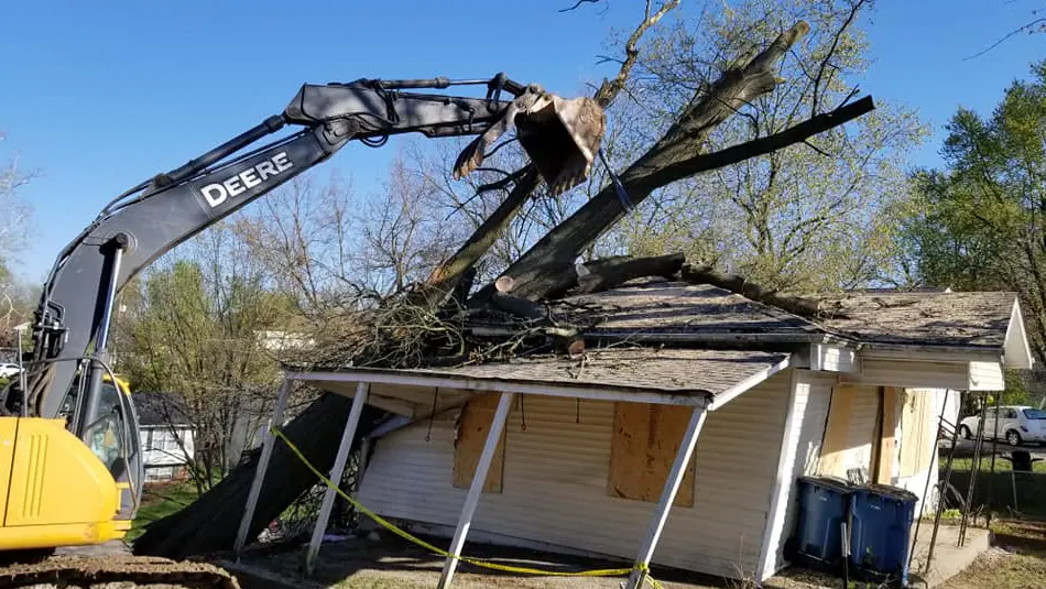 Excavator removing fallen tree from damaged house roof during emergency tree removal in Collinsville, IL